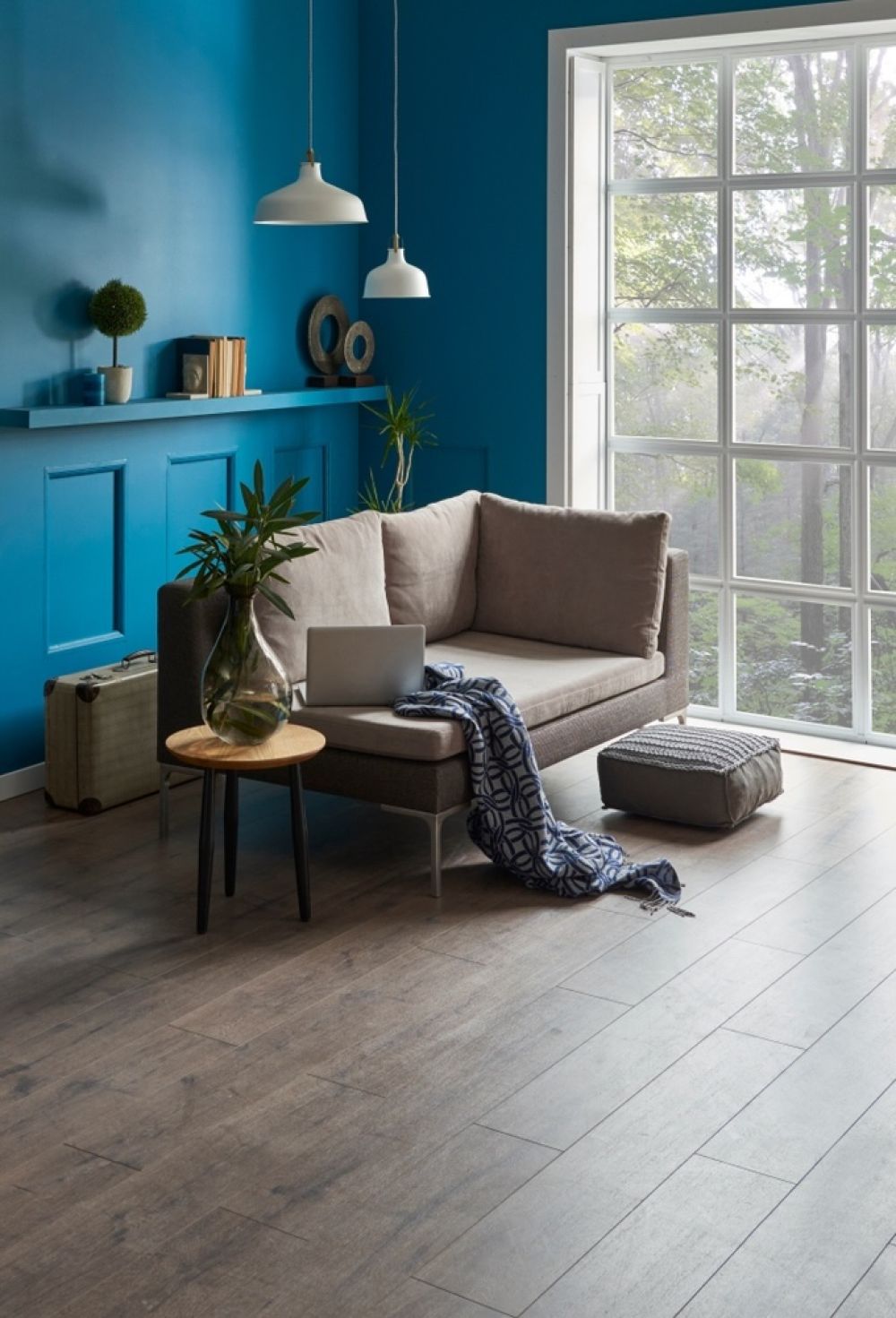 This corner demonstrates the power of simple yet functional design in maximizing comfort. A neutral-toned sofa, complemented by a cozy throw and natural light from the large windows, shows how even small spaces can be transformed into a peaceful retreat with the right furniture placement.