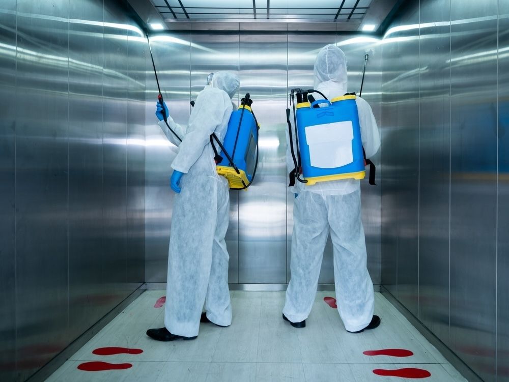 Technicians applying electrostatic spraying for effective sanitization inside an elevator.