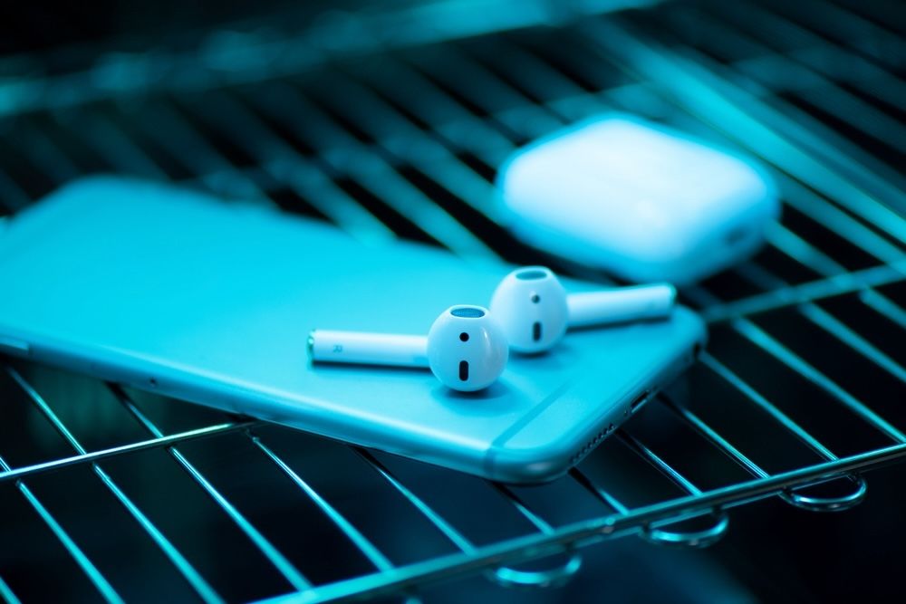 A UV-C sterilization device disinfects a smartphone and earbuds, highlighting the technology's versatility for everyday items. This chemical-free method ensures personal electronics are free from harmful pathogens, promoting better hygiene.