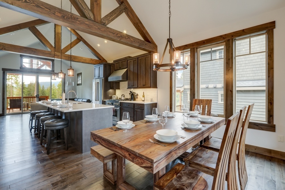 Rustic Dining - Capturing the essence of rustic elegance, this dining space boasts a sturdy wooden table and a modern kitchen backdrop. The open beam ceiling and large windows offer an expansive outdoor view, merging the comforts of home with the grandeur of nature.